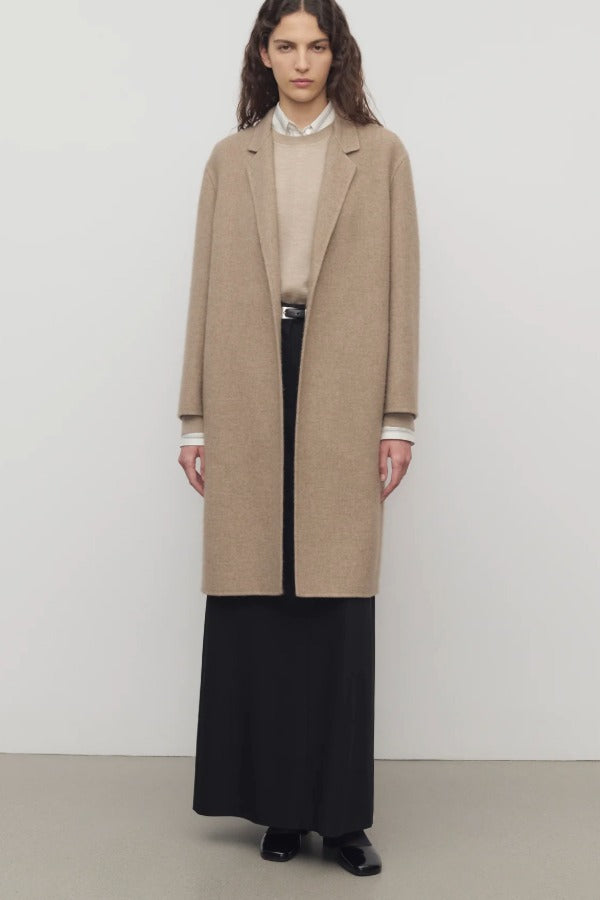 Front view of natural fedra coat on model wearing beige top, black skirt and mules, against a white background.