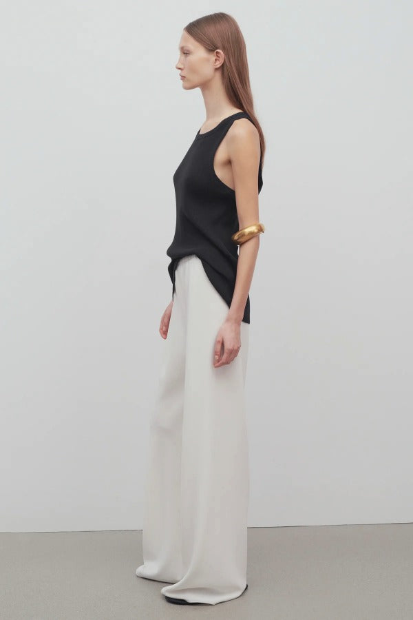 Side view of off white gala pant on model wearing black tank top, against a white background.