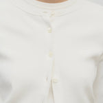A model wears a long-sleeved white cotton button-down cardigan over a crew neck white t-shirt. The viewpoint is a closeup of the model from the front.