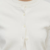 A model wears a long-sleeved white cotton button-down cardigan over a crew neck white t-shirt. The viewpoint is a closeup of the model from the front.