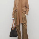 Front view of dark sand igor pant on model wearing camel sweater and boots, against a white background.