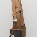 Side view of dark sand igor pant on model wearing camel sweater and boots, against a white background.