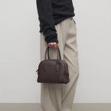 Front view of deep brown india 10 bag on model wearing black sweater, khaki pants and mules, against a white background.