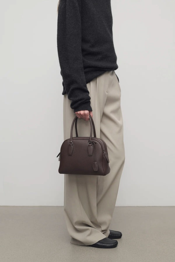 Front view of deep brown india 10 bag on model wearing black sweater, khaki pants and mules, against a white background.