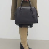 Front view of black india 12 bag on model wearing khaki trench coat and heels, against a white background.