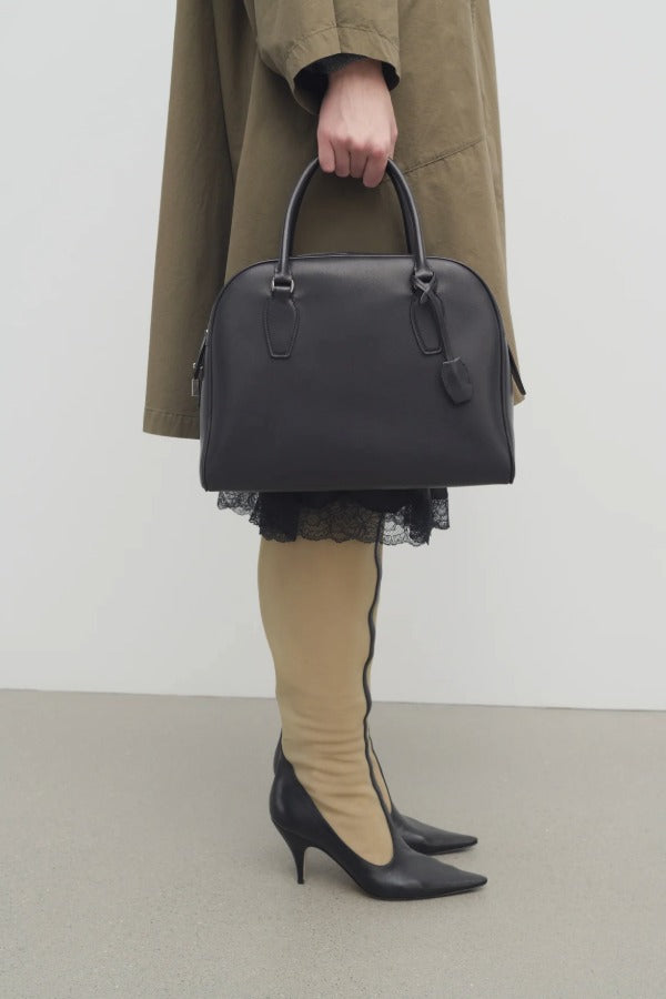 Front view of black india 12 bag on model wearing khaki trench coat and heels, against a white background.