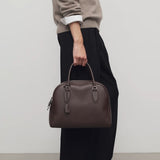 Front view of deep brown india 12 bag on model wearing black pants, taupe sweater and loafers, against a white background.