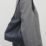 Front view of blu notte isa shoulder bag on model wearing grey coat, against a white background.