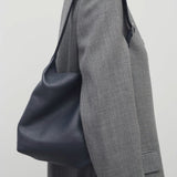 Front view of blu notte isa shoulder bag on model wearing grey coat, against a white background.