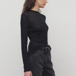 Side view of black iverness top on model wearing black jeans and belt, against a white background.