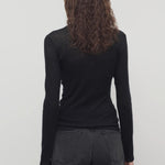 Back view of black iverness top on model wearing black jeans and belt, against a white background.