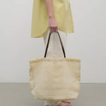 Front view of the ivory mesh and leather bag is pictured on a white background, shown with model wearing white trousers and yellow shirt with sandals.
