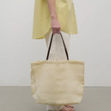 Front view of the ivory mesh and leather bag is pictured on a white background, shown with model wearing white trousers and yellow shirt with sandals.