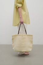Front view of the ivory mesh and leather bag is pictured on a white background, shown with model wearing white trousers and yellow shirt with sandals.