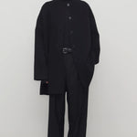 Front view of black kala coat on model wearing black turtleneck and trousers, against a white background.