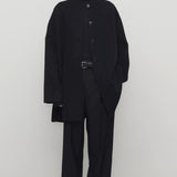 Front view of black kala coat on model wearing black turtleneck and trousers, against a white background.