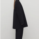 Side view of black kala coat on model wearing black turtleneck and trousers, against a white background.