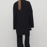 Back view of black kala coat on model wearing black turtleneck and trousers, against a white background.