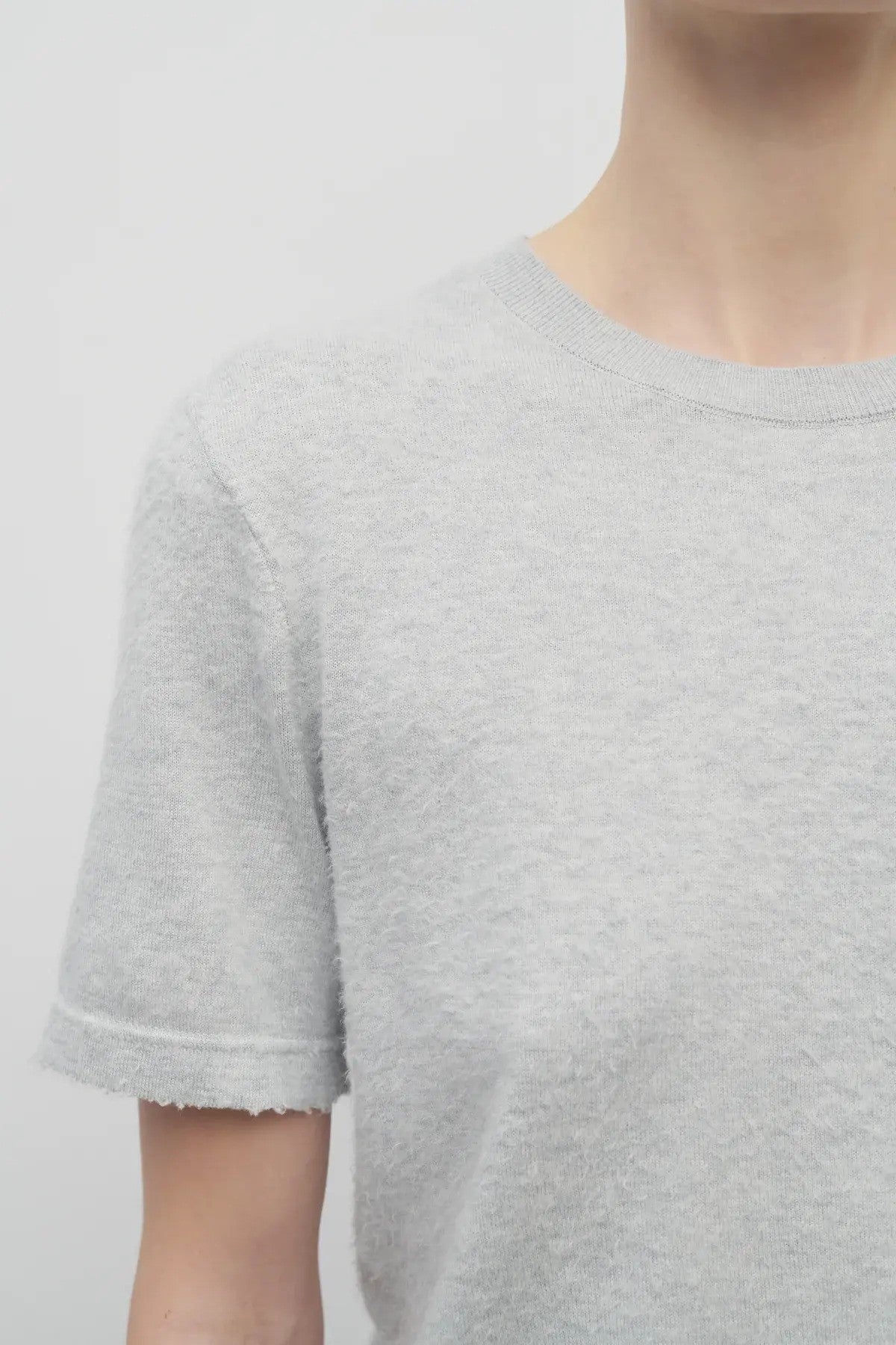 A closeup of the model wearing a short sleeve cotton grey melange t-shirt with white backdrop.