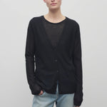 A model with light brown hair is shown wearing the black long sleeve knit cardigan with button down closure over a crew neck t-shirt and baggy jeans. Viewpoint is frontside with a white backdrop.