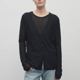 A model with light brown hair is shown wearing the black long sleeve knit cardigan with button down closure over a crew neck t-shirt and baggy jeans. Viewpoint is frontside with a white backdrop.