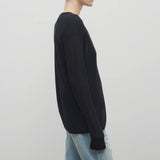 A model with light brown hair wears a long sleeve black knit cardigan with baggy jeans shown at a side angle against a white backdrop.