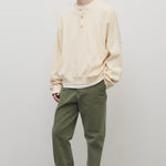 Front slanted view of khaki green pants on model wearing white button down sweatshirt and white shoes, against white background.