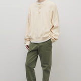 Front slanted view of khaki green pants on model wearing white button down sweatshirt and white shoes, against white background.