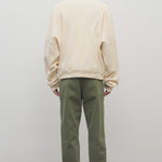 Back view of khaki green pants on model wearing white sweatshirt and white shoes, against white background.