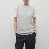 A model with dark brown hair is shown in the sleeveless knit top and navy trousers with frontside viewpoint on white backdrop