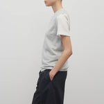 A model with dark brown hair wears the sleeveless knit top in grey melange worn with navy trousers shown at a side angle against a white backdrop