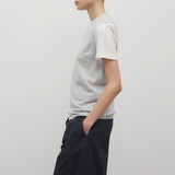 A model with dark brown hair wears the sleeveless knit top in grey melange worn with navy trousers shown at a side angle against a white backdrop
