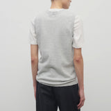 A model with dark brown hair wears the sleeveless knit top in grey melange with navy trousers show backside against a white backdrop.