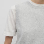 A model wears the sleeveless knit top in grey melange on top of a cotton short sleeve white t-shirt.