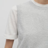 A model wears the sleeveless knit top in grey melange on top of a cotton short sleeve white t-shirt.
