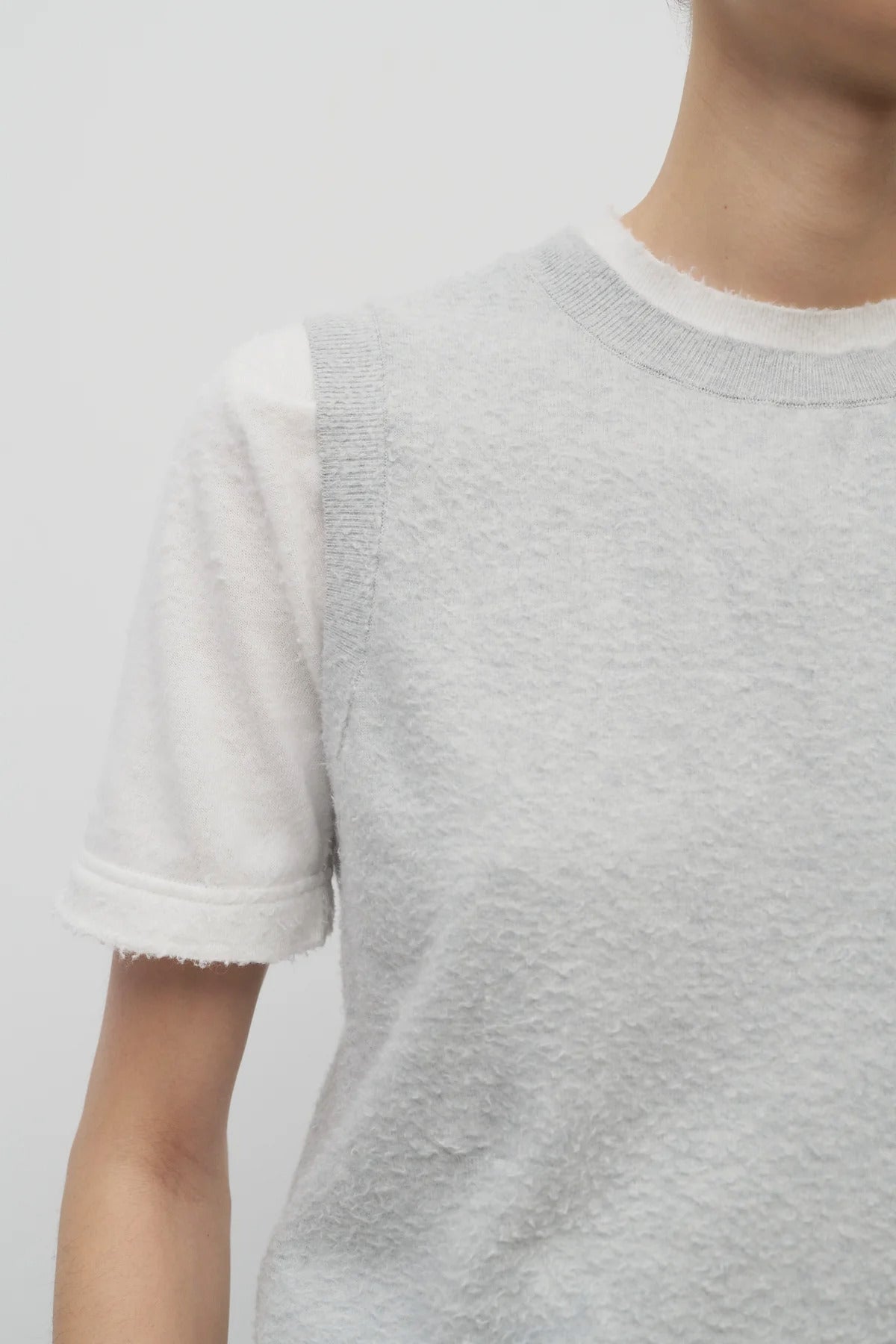 A model wears the sleeveless knit top in grey melange on top of a cotton short sleeve white t-shirt.