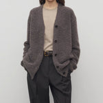 Front view of taupe laleh cardigan on model wearing beige top and charcoal pants, against a white background.