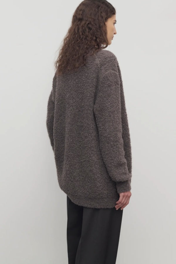 Back view of taupe laleh cardigan on model wearing charcoal pants, against a white background.
