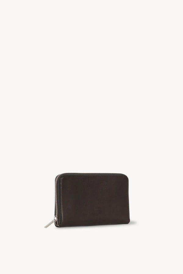 Side slanted view of dark brown large zip wallet on white background, with no model shown.