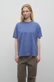 A model with long blonde hair is shown in the light blue cotton t-shirt worn with khaki trousers and frontside viewpoint against a white backdrop.