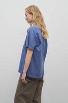 A model with long blonde hair is shown at a side angle in the light blue cotton t-shirt worn with khaki trousers against a white backdrop