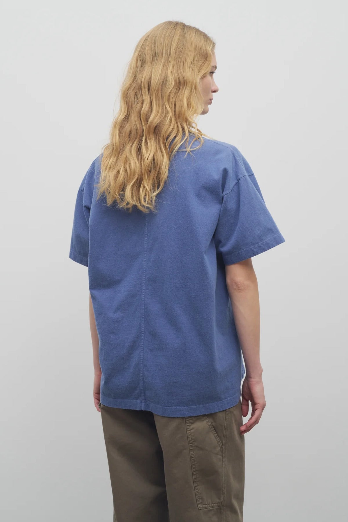 A model with long blonde hair wears the light blue cotton t-shirt with khaki trousers and shown backside angle against a white backdrop