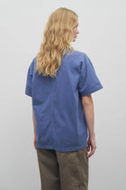 A model with long blonde hair wears the light blue cotton t-shirt with khaki trousers and shown backside angle against a white backdrop