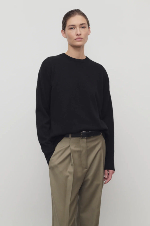 Front view of black leilani top on model wearing khaki pants with black belt, against white background.