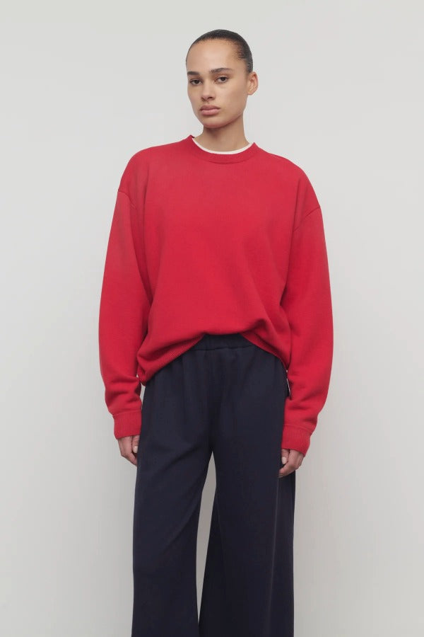 Front view of red leora sweatshirt on model wearing navy pants, against a white background.