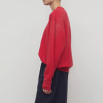 Side view of red leora sweatshirt on model wearing navy pants, against a white background.