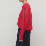 Side view of red leora sweatshirt on model wearing navy pants, against a white background.