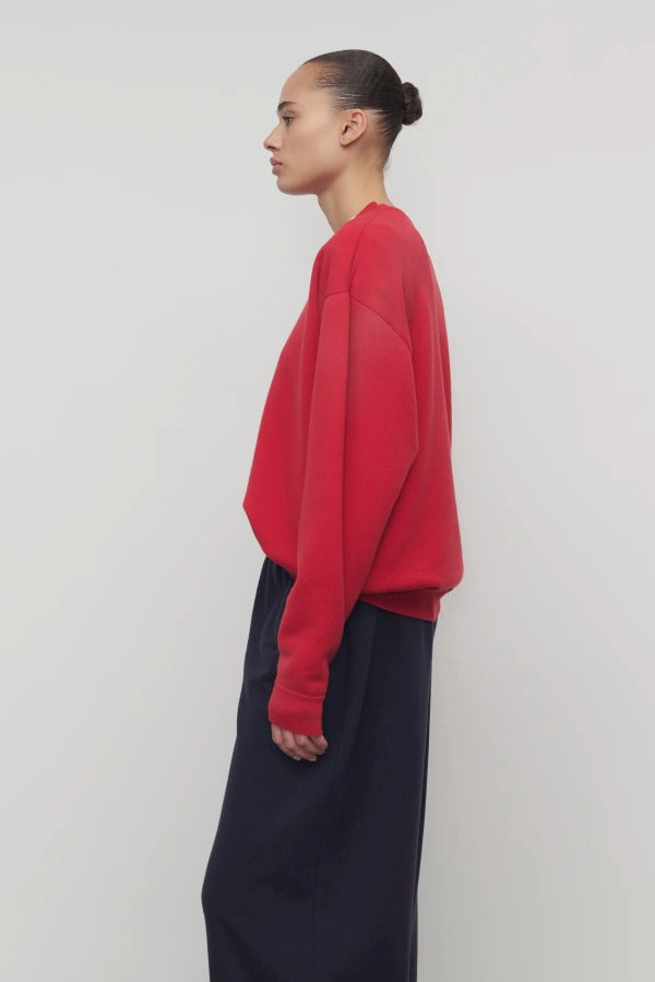 Side view of red leora sweatshirt on model wearing navy pants, against a white background.