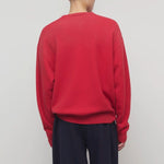 Back view of red leora sweatshirt on model wearing navy pants, against a white background.