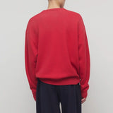Back view of red leora sweatshirt on model wearing navy pants, against a white background.